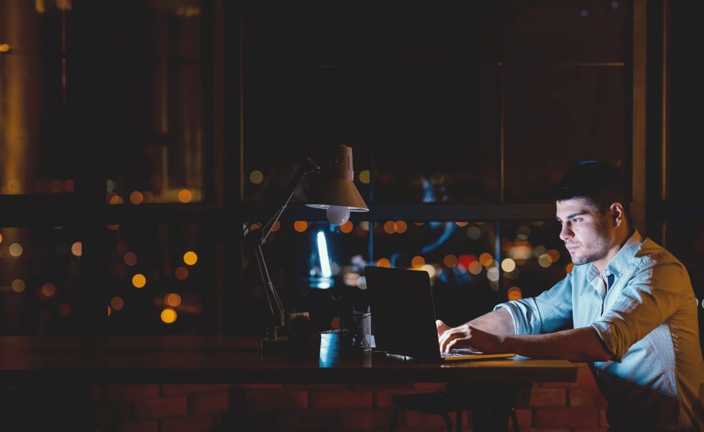 Makler bei Nachtarbeit am Laptop als Symbol für Belastung und Bestandsverkauf